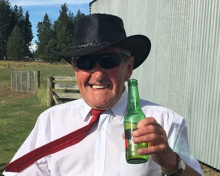 Man outdoors wearing hat, sunglasses, holding drink.