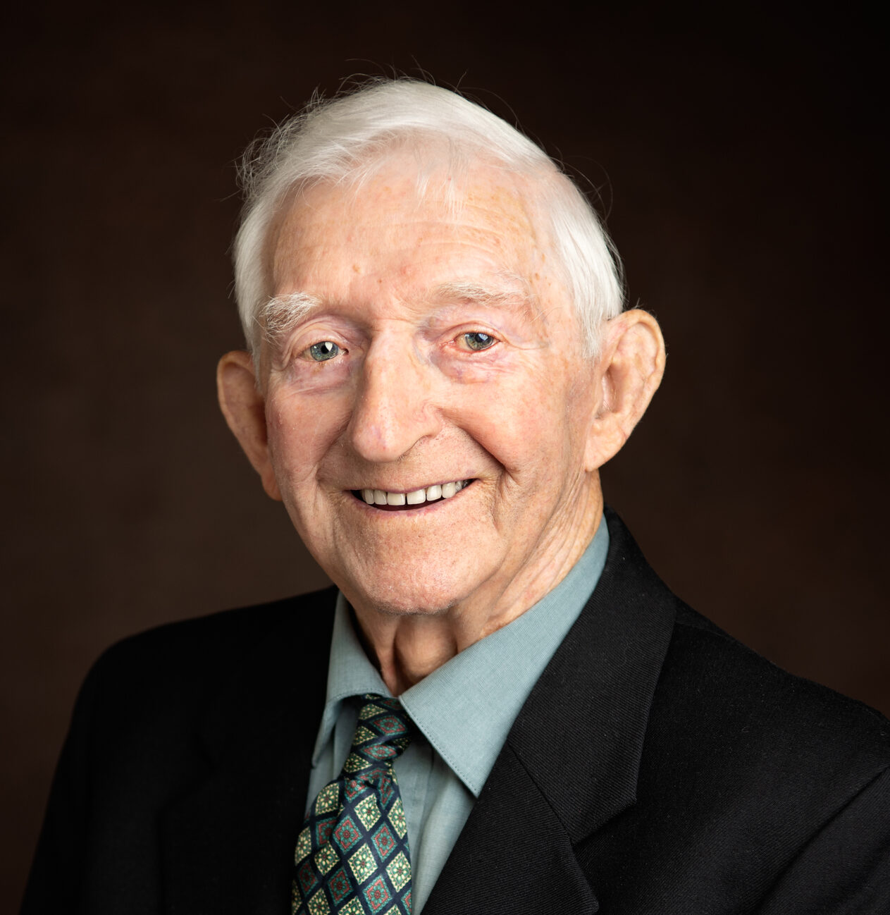 Elderly man in suit and tie, smiling.