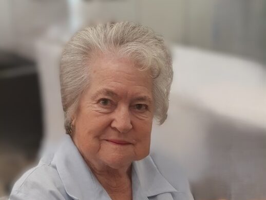 Senior woman smiling in blue shirt, holding bag handle.