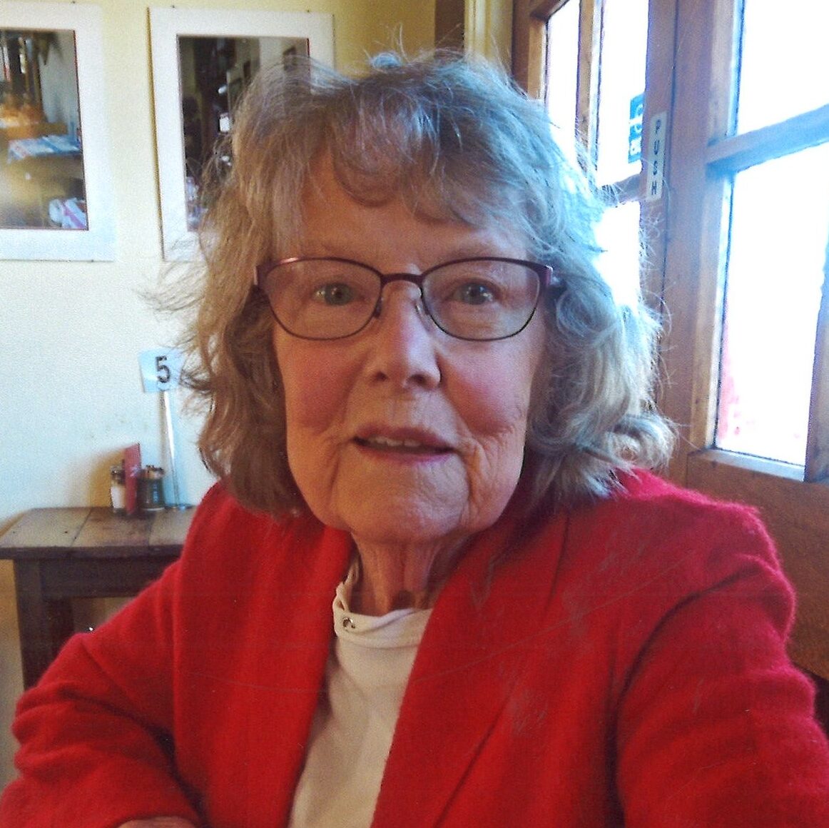 Smiling woman in red jacket sitting at table.