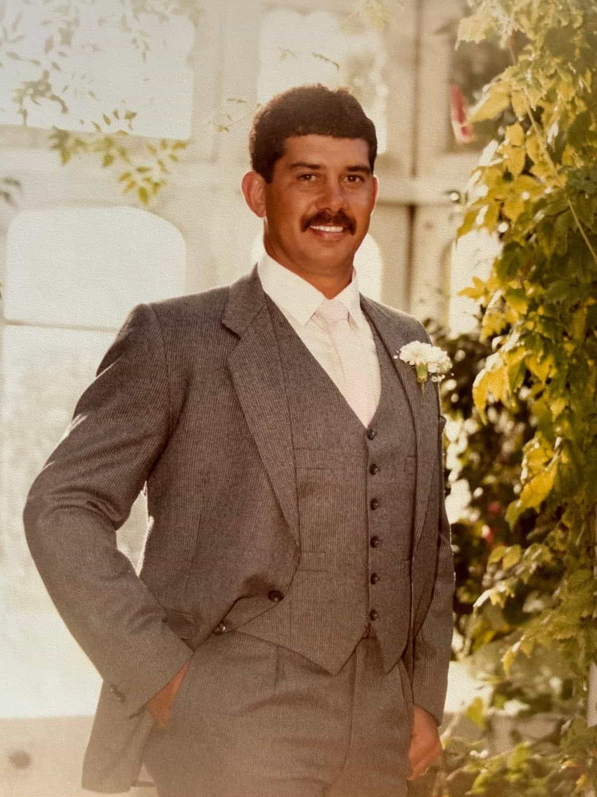 Man in grey suit with plants indoors.