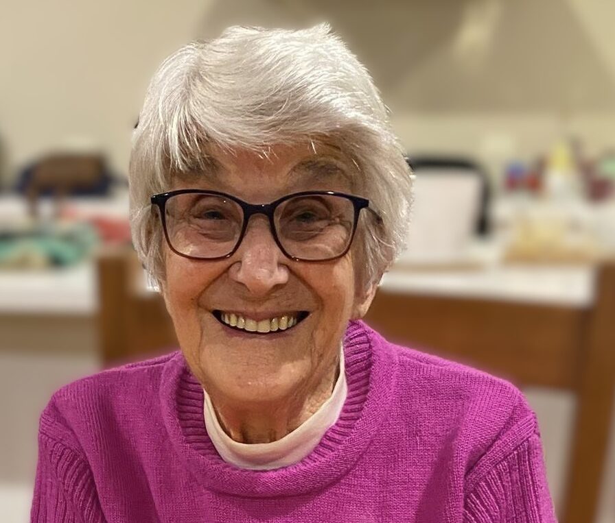Smiling elderly woman in pink with candle-lit table.