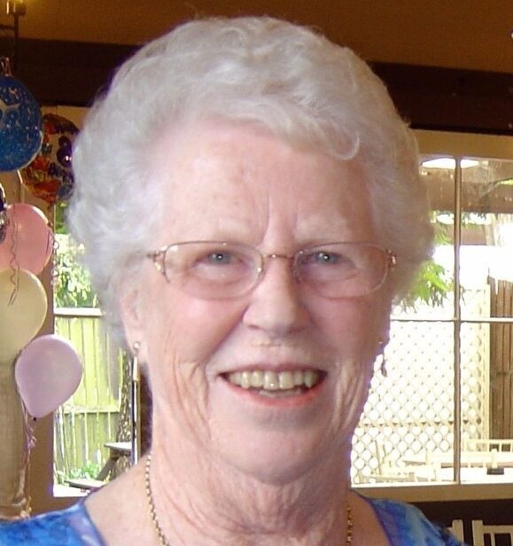 Smiling woman at party with balloons, wearing blue top.