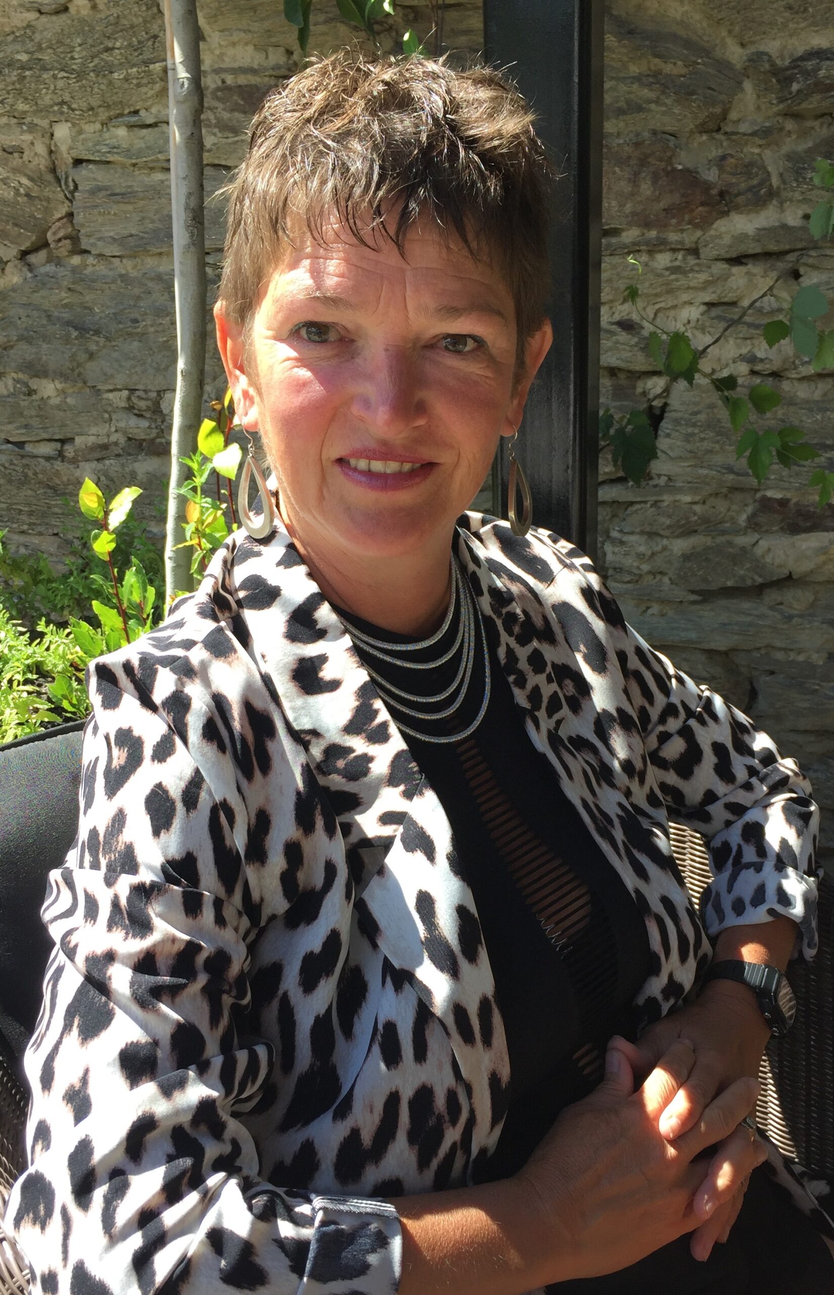 Woman in leopard jacket outdoors, smiling.